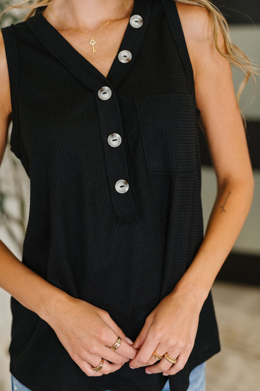 Black sleeveless top with silver buttons worn by a person, blurred background