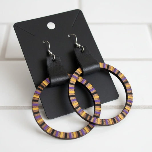 Pair of hoop earrings with purple and gold accents on a dark background