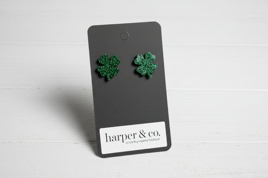 Green four-leaf clover earrings on a 'harper & co.' card against a teal background