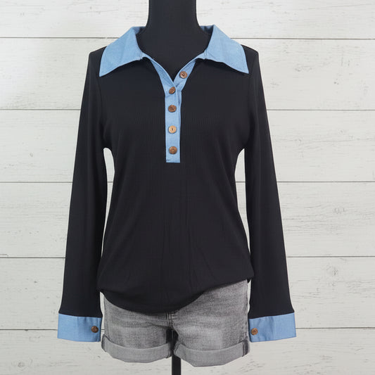 Black long-sleeve shirt with blue collar and cuffs on a mannequin against a light wooden background