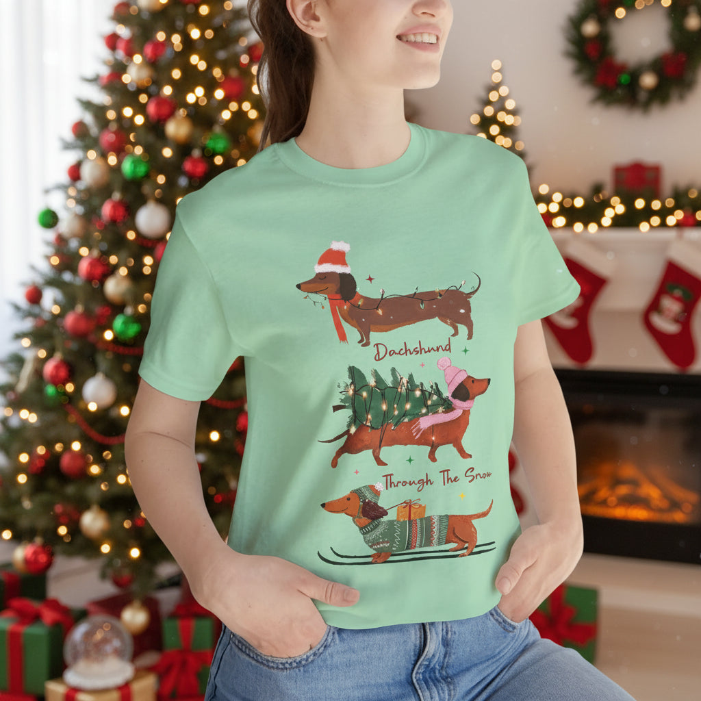 Person wearing a light green t-shirt with Christmas-themed dachshund illustrations.