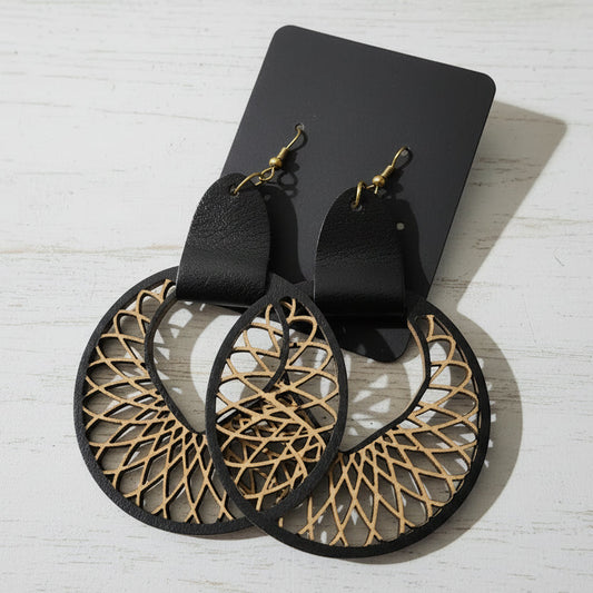 Pair of black earrings with gold geometric patterns on a wooden surface