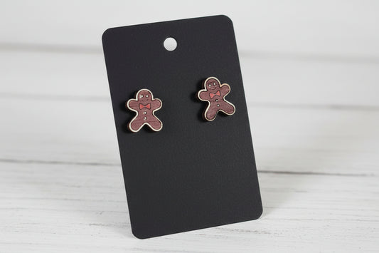 Two gingerbread man-shaped earrings on a black card with a wooden surface.