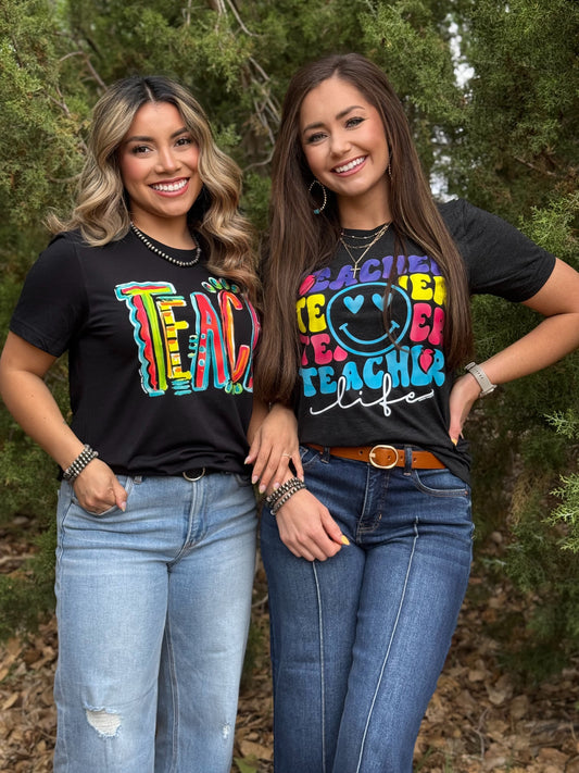 Two women wearing black t-shirts with colorful text and graphics, standing outdoors.