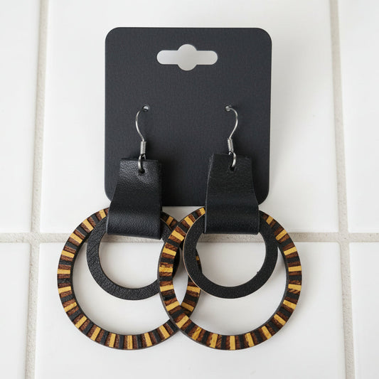 Pair of hoop earrings with black leather straps and wooden accents on a dark surface.