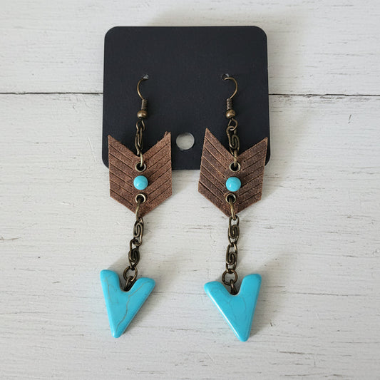Pair of earrings with brown chevron design and turquoise stones on a wooden surface.