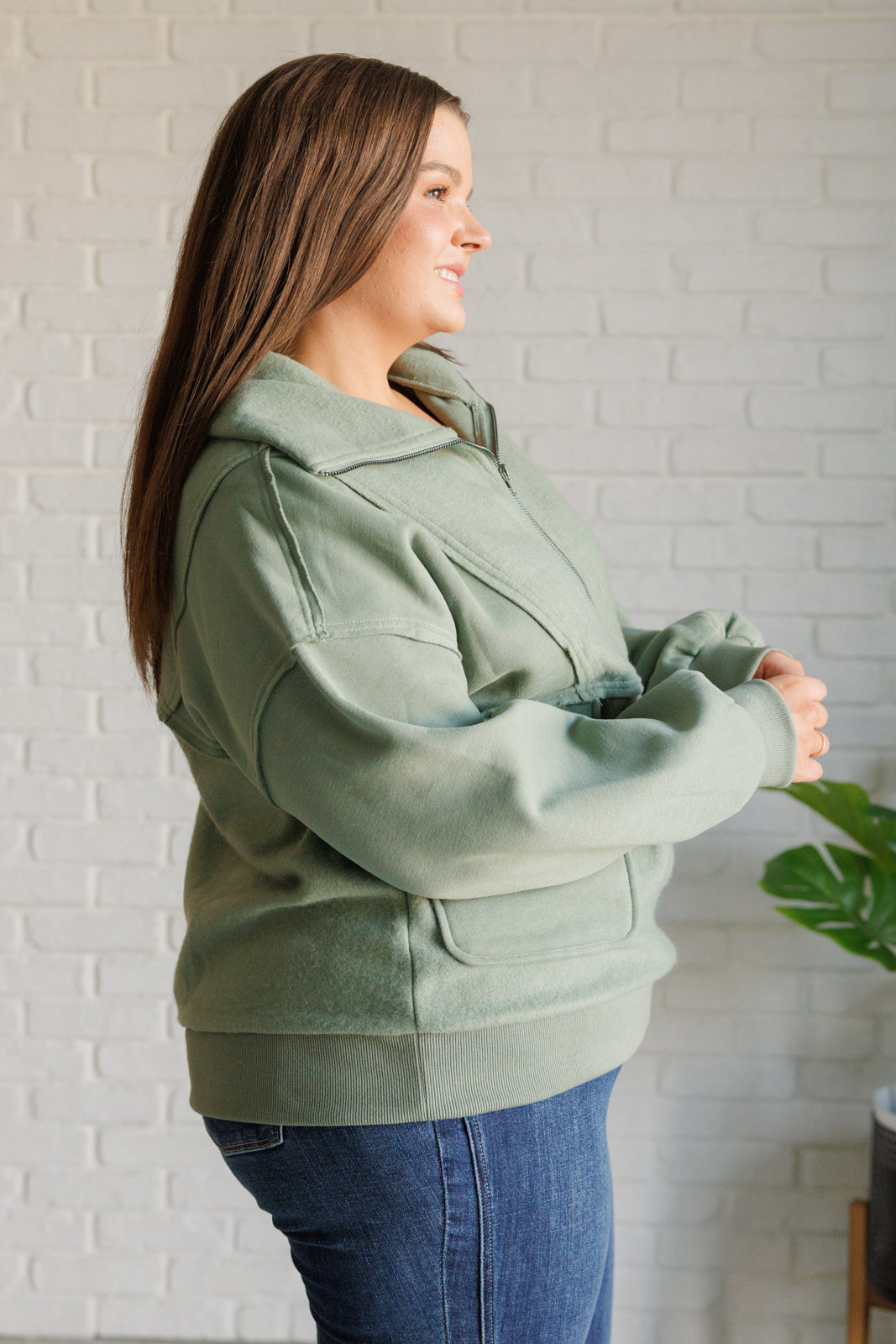 Woman wearing a green jacket standing against a white brick wall.