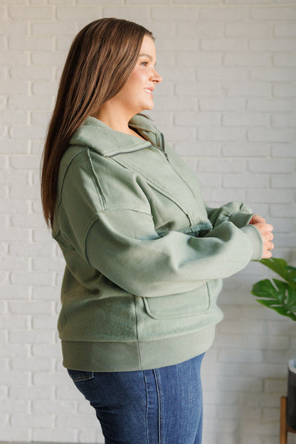 Woman wearing a green jacket standing against a white brick wall.