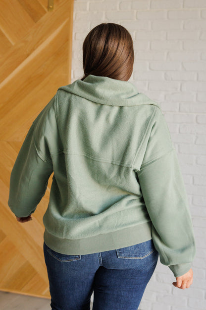 Person wearing a green hoodie standing against a white brick wall.