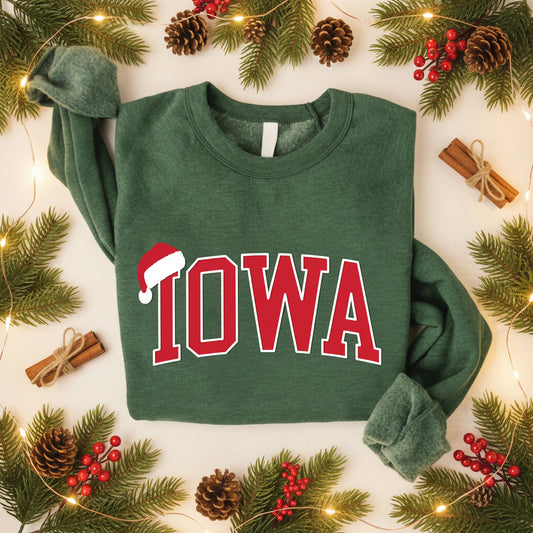 A dark green long-sleeve sweatshirt with 'IOWA' printed in red varsity letters outlined in white across the chest, with a small Santa hat graphic replacing the letter A. The sweatshirt is laid flat on a white background with a 'PUFF PRINT' logo in the bottom right corner.